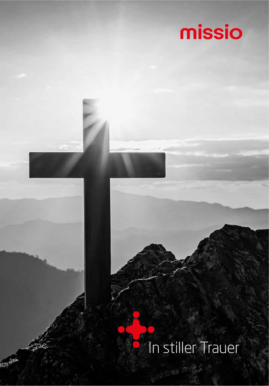 Schwarz-weißes Symbolbild mit Kreuz auf einem Berggipfel, missio-Logo und  Schriftzug In stiller Trauer