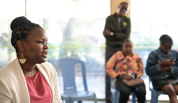 In einem Raum sitzt im Vordergrund missio-Projektpartnerin Winnie Mutevu bei einem Workshop und spricht in die Runde. Im Hintergrund verschwommen sieht man zwei sitzende Frauen und einen stehenden Mann.