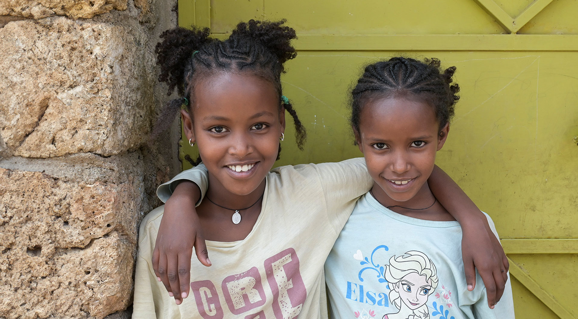 Emebet (rechts im Bild) und ihre Freundin Arsema stehen Arm in Arm vor dem Eingang des Waisenhauses in Harar. Beide lächeln.