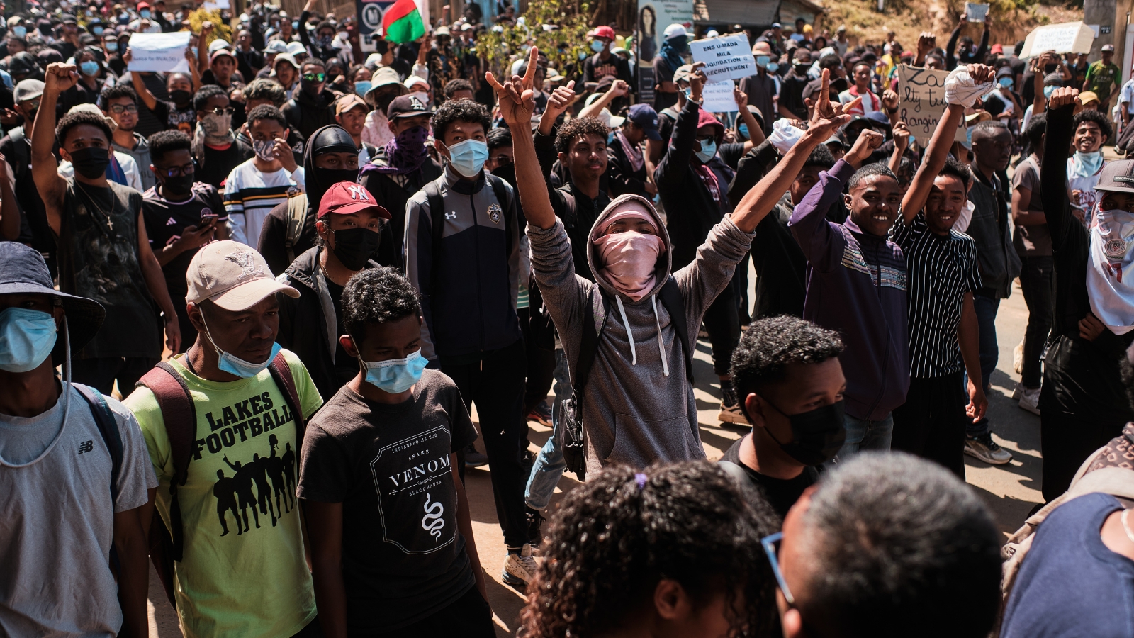 Eine Gruppe protestierender junger Madagassen. Prominent in der Mitte des Bildes läuft ein junger Mann in grauem Hoodie, das Gesicht bis auf die Augen mit einem rosa Tuch verhüllt. Er reißt die Arme kämpferisch nach oben. Foto: iAko Randrianarivelo