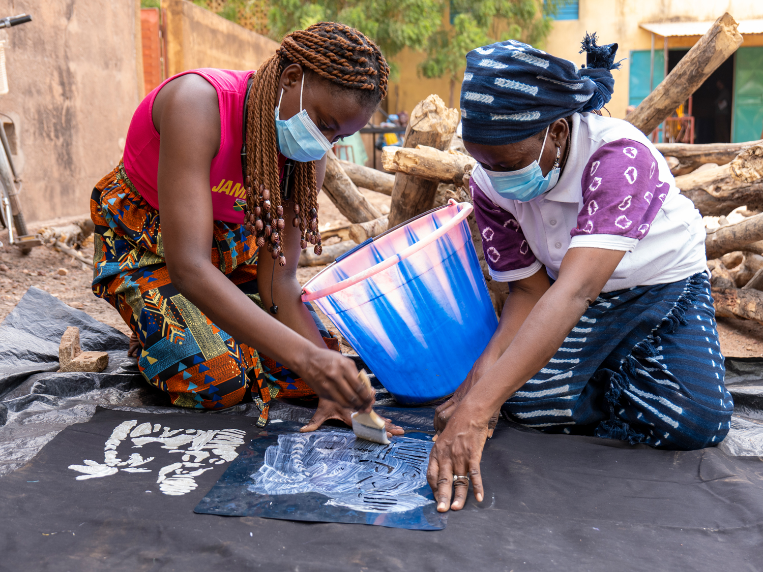 Zwei Frauen knien auf dem Boden und gestalten gemeinsam eine Batik-Arbeit in schwarz-weiß.