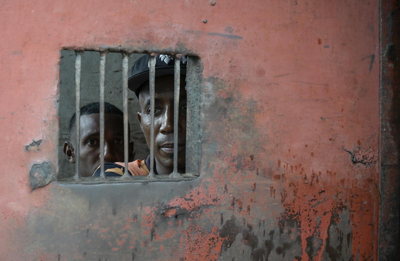 Zwei Gefangene blicken in einem Gefängnis in Madagaskar von ihrer Zelle durch ein kleines vergittertes Fenster nach draußen.