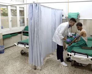 Ein junger Mann sitzt auf einem Krankenbett. Er wird von einem vor ihm stehenden Arzt versorgt