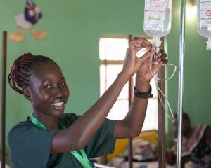Eine junge Krankenschwester aus dem Südsudan schließt eine Infusionskanüle an und lacht in die Kamera.