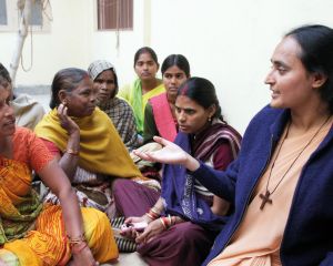Eine junge Ordensschwester aus Indien spricht mit einer Frau in buntem Gewand, die ihr gegenüber auf dem Boden sitzt. Neben ihnen weitere Frauen unterschiedlichen Alters.