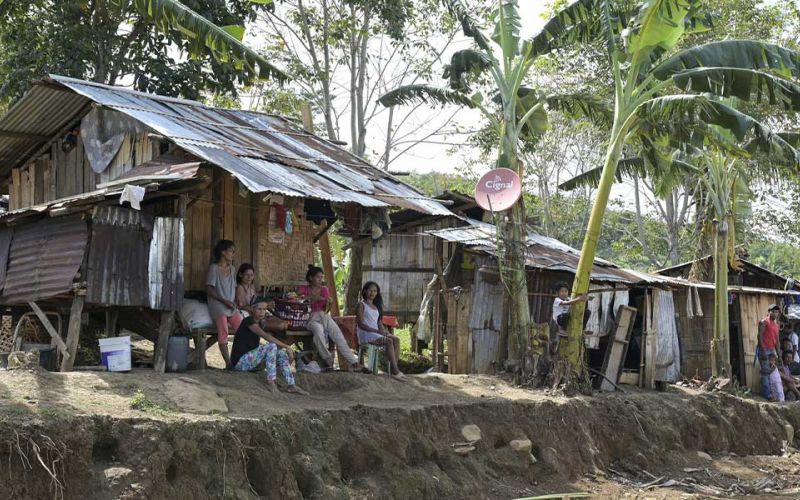 Menschen sitzen auf der philippinischen Insel Mindanao vor ihren ärmlichen mit Wellblech bedeckten Behausungen. Dazwischen wachsen Palmen.